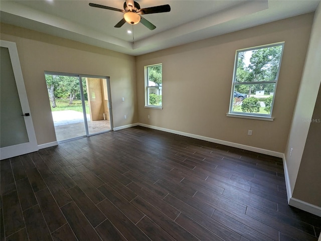 spare room with a tray ceiling, a ceiling fan, dark wood-style flooring, and baseboards