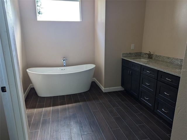 bathroom with a freestanding bath, vanity, baseboards, and wood tiled floor