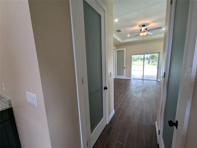 hallway with visible vents, baseboards, wood finish floors, a textured ceiling, and a raised ceiling