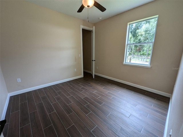 empty room featuring dark wood-style floors, a ceiling fan, and baseboards