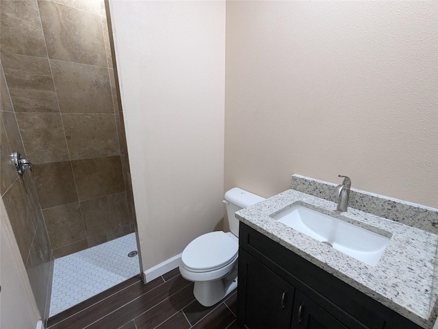 full bath with vanity, wood finished floors, baseboards, a tile shower, and toilet