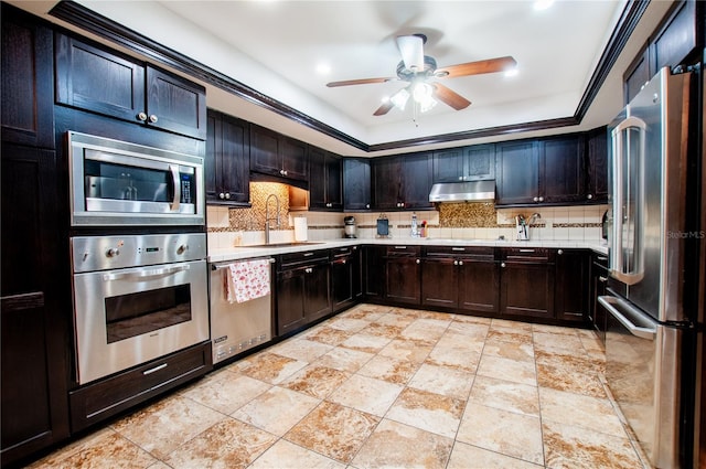 kitchen featuring tasteful backsplash, a raised ceiling, stainless steel appliances, light countertops, and under cabinet range hood