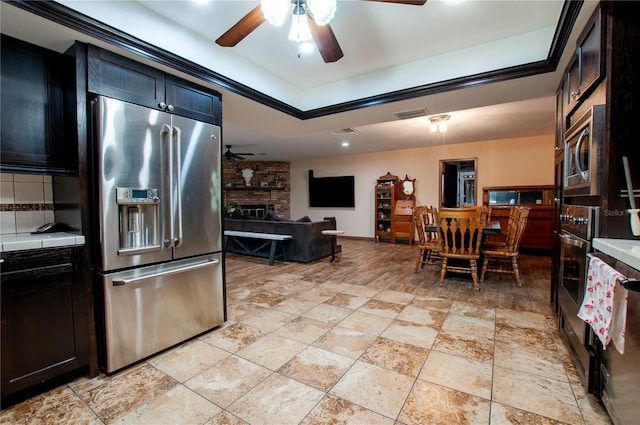 kitchen featuring light tile patterned floors, a fireplace, ceiling fan, stainless steel appliances, and brick wall