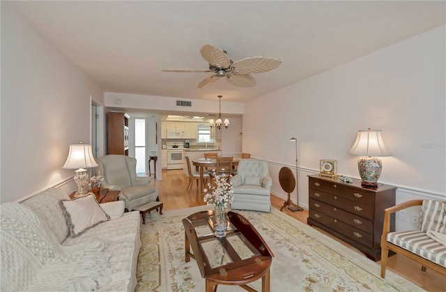 living room with light wood-type flooring and ceiling fan with notable chandelier