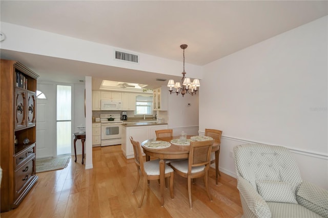 dining room with sink, light wood-type flooring, and an inviting chandelier