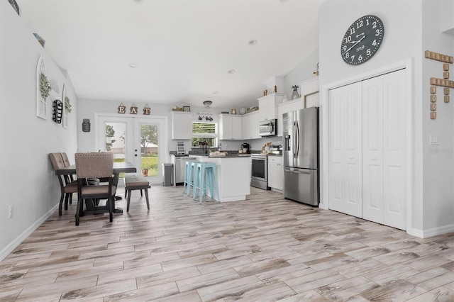 kitchen with white cabinets, french doors, appliances with stainless steel finishes, a breakfast bar area, and a center island