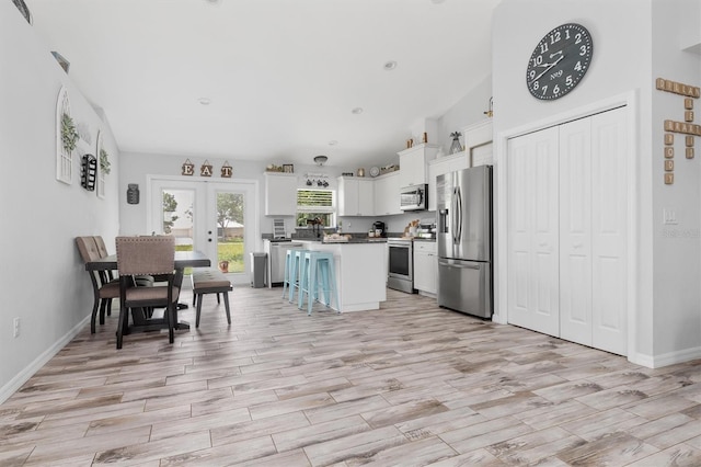 kitchen with a kitchen island, white cabinets, french doors, appliances with stainless steel finishes, and a kitchen bar