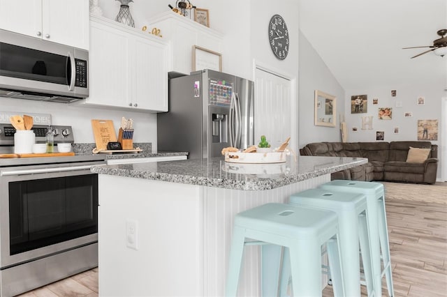 kitchen featuring stainless steel appliances, a breakfast bar, open floor plan, and white cabinetry