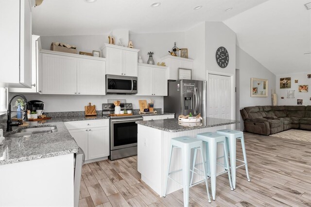 kitchen featuring stainless steel appliances, a sink, white cabinets, and a center island