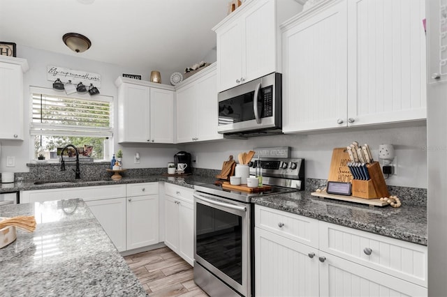 kitchen with sink, dark stone countertops, light hardwood / wood-style floors, stainless steel appliances, and white cabinets