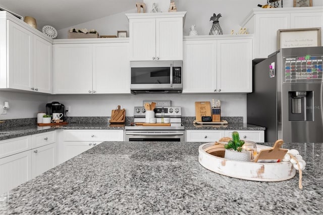 kitchen with appliances with stainless steel finishes, vaulted ceiling, white cabinets, and dark stone counters