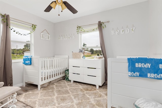 bedroom with ceiling fan, a crib, light hardwood / wood-style floors, and multiple windows