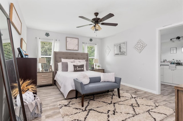 bedroom with baseboards, connected bathroom, light wood finished floors, and ceiling fan