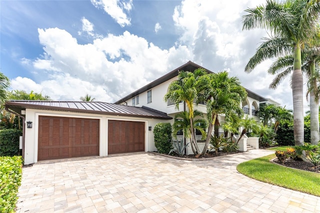 view of front of property with a garage, metal roof, a standing seam roof, decorative driveway, and stucco siding