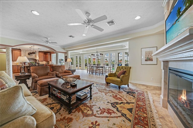 living area featuring a glass covered fireplace, visible vents, crown molding, and baseboards