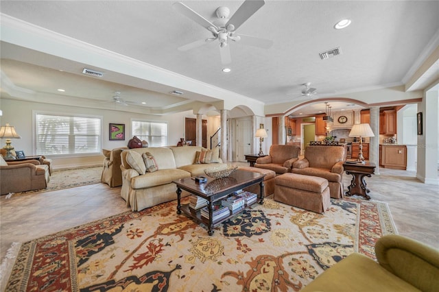 living area featuring visible vents, arched walkways, a raised ceiling, crown molding, and ornate columns