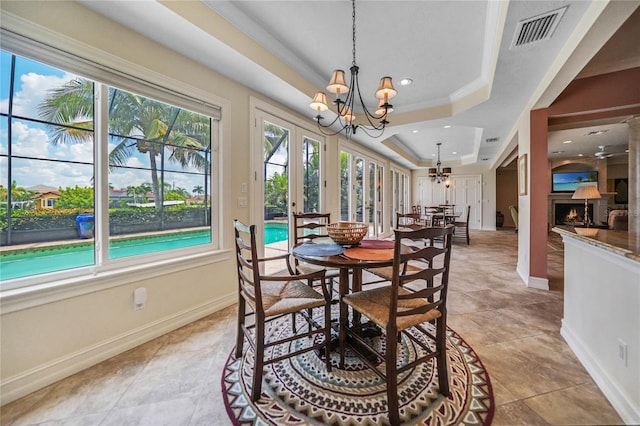 dining space with a warm lit fireplace, visible vents, baseboards, a tray ceiling, and a chandelier