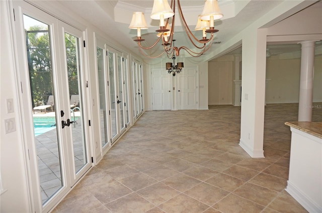 unfurnished sunroom featuring decorative columns, a chandelier, a raised ceiling, and french doors