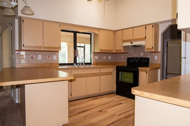 kitchen featuring sink, a high ceiling, black range with electric cooktop, light hardwood / wood-style flooring, and kitchen peninsula