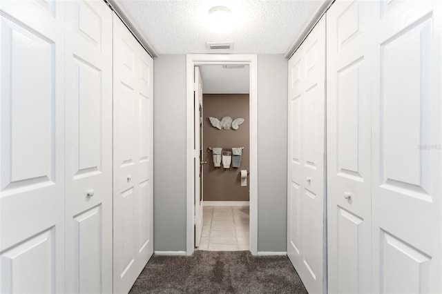 corridor featuring a textured ceiling and dark carpet