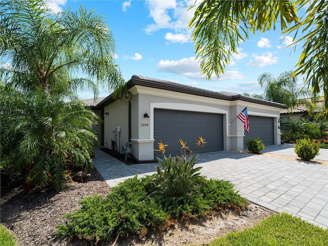 ranch-style house with a garage, decorative driveway, a tile roof, and stucco siding