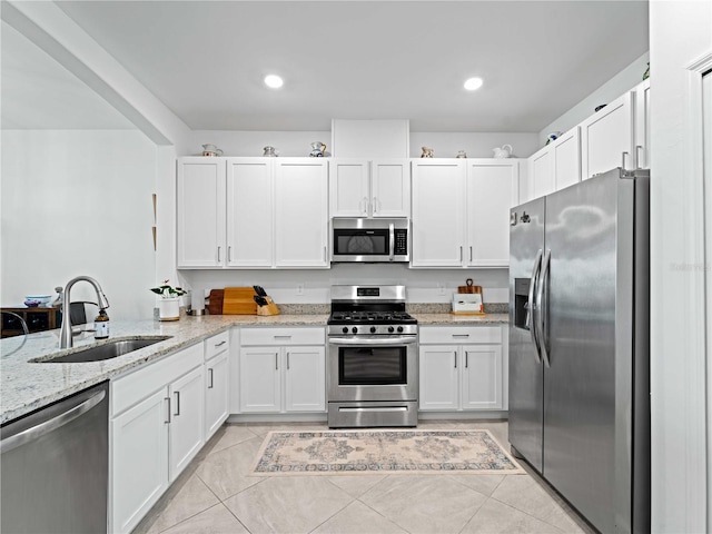 kitchen with stainless steel appliances, white cabinetry, sink, light stone countertops, and light tile patterned floors