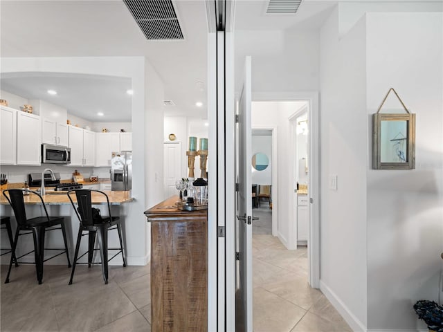 kitchen featuring stainless steel appliances, visible vents, a kitchen bar, and white cabinetry