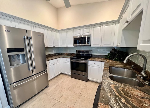 kitchen with tasteful backsplash, white cabinets, dark stone counters, stainless steel appliances, and a sink