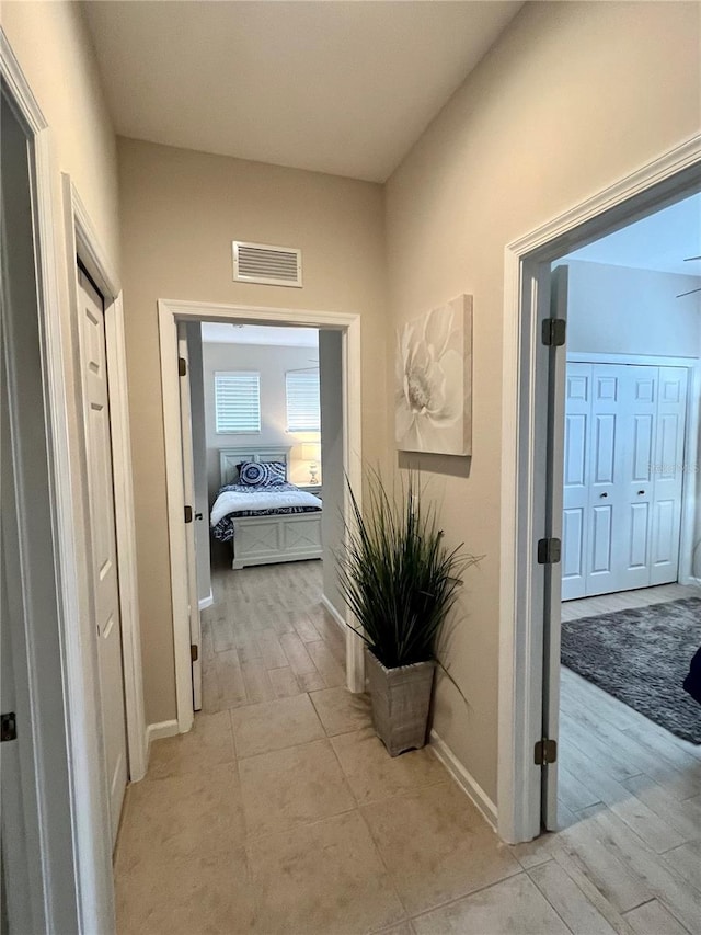 hall with light wood-type flooring, visible vents, and baseboards