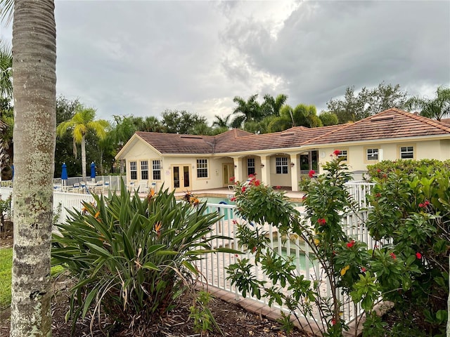 rear view of house with a patio, a community pool, fence, french doors, and stucco siding