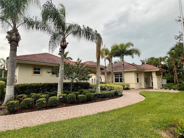 mediterranean / spanish home with a tiled roof, a front lawn, and stucco siding