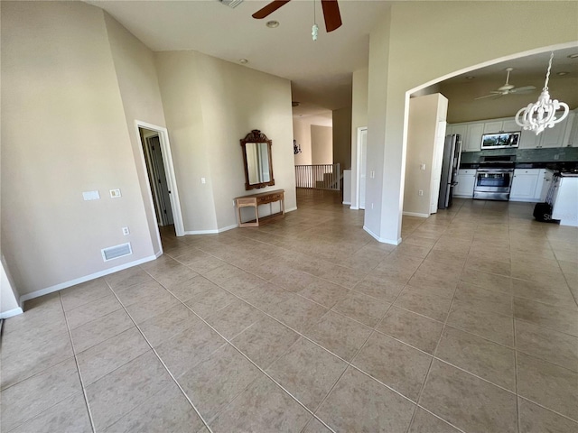 unfurnished living room featuring ceiling fan with notable chandelier, a towering ceiling, and light tile patterned floors