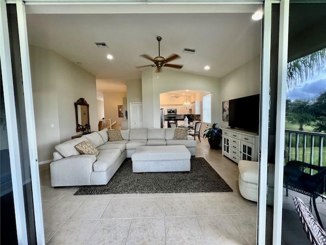 living room featuring ceiling fan with notable chandelier, light tile patterned flooring, and vaulted ceiling