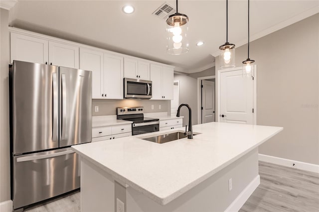 kitchen featuring stainless steel appliances, a center island with sink, ornamental molding, and light wood-type flooring