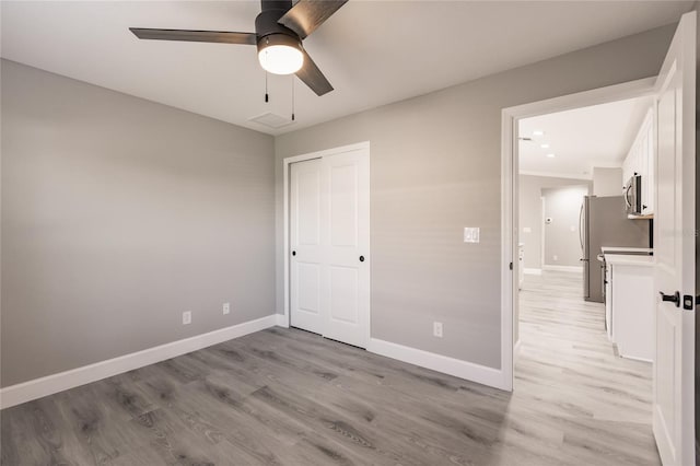 unfurnished bedroom with light wood-style floors, a closet, freestanding refrigerator, and baseboards