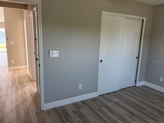 unfurnished bedroom featuring baseboards, wood finished floors, and a closet