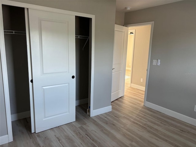 unfurnished bedroom featuring light wood finished floors, baseboards, and a closet