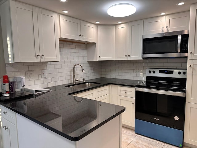 kitchen with stainless steel appliances, white cabinetry, light tile patterned floors, and dark stone countertops