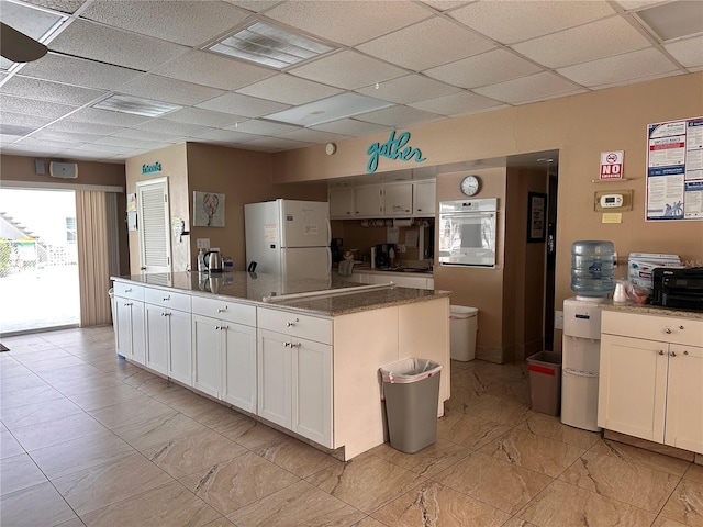 kitchen with wall oven, white refrigerator, light tile patterned flooring, and a drop ceiling