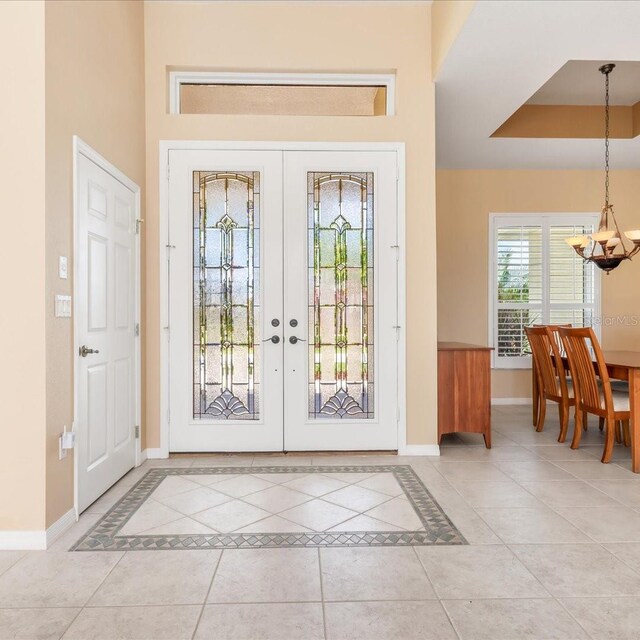 interior space featuring a tray ceiling, light tile patterned flooring, an inviting chandelier, and french doors