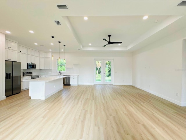 kitchen featuring white cabinets, light hardwood / wood-style flooring, a kitchen island, a tray ceiling, and appliances with stainless steel finishes