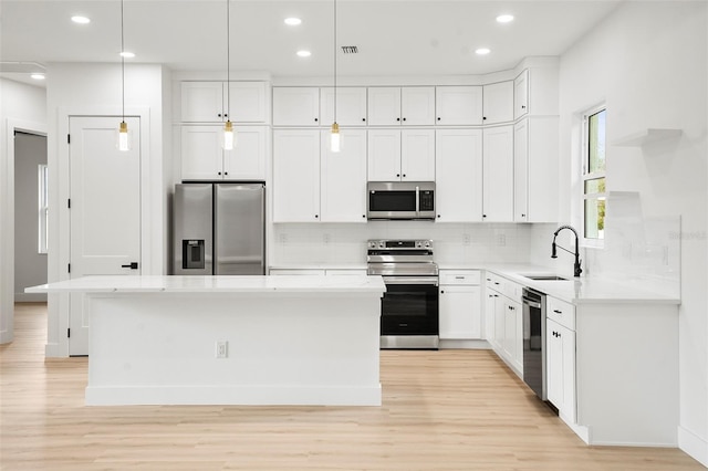 kitchen with a kitchen island, appliances with stainless steel finishes, decorative light fixtures, sink, and white cabinets