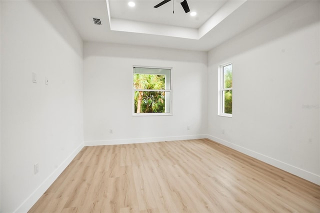 spare room with light wood-type flooring, a tray ceiling, and ceiling fan