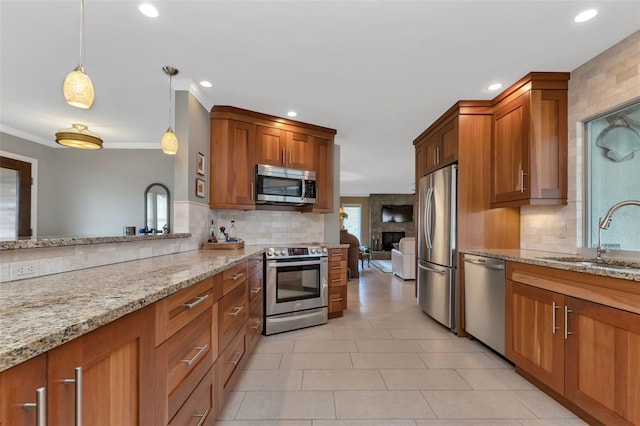 kitchen with light stone countertops, stainless steel appliances, crown molding, sink, and decorative light fixtures