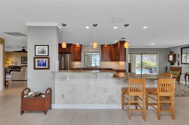 kitchen featuring kitchen peninsula, stainless steel fridge, light stone counters, decorative light fixtures, and a breakfast bar area