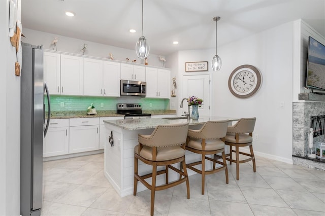 kitchen with pendant lighting, an island with sink, stainless steel appliances, sink, and white cabinets