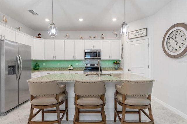 kitchen featuring a kitchen breakfast bar, appliances with stainless steel finishes, a kitchen island with sink, decorative backsplash, and white cabinetry