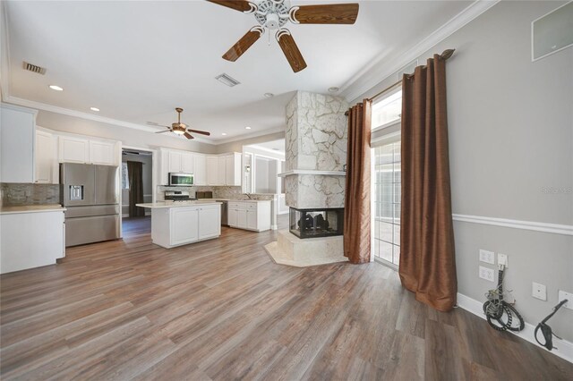 unfurnished living room with ceiling fan, light hardwood / wood-style flooring, ornamental molding, sink, and a fireplace