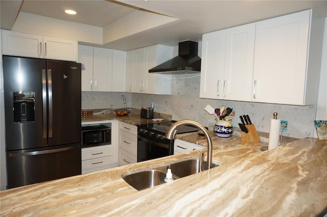 kitchen with light stone countertops, fridge with ice dispenser, sink, white cabinetry, and wall chimney range hood