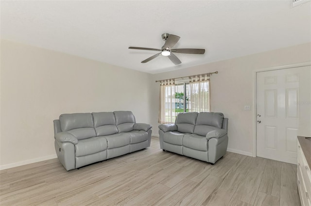 living room featuring a ceiling fan, baseboards, and light wood finished floors